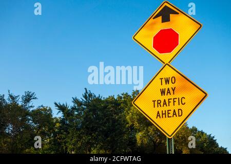 two way traffic ahead sign with ted stop sign icon and arrow trees and blue shy in background Stock Photo