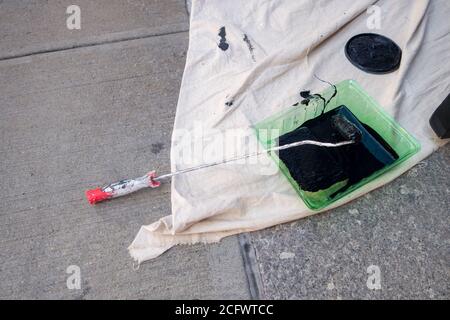 Black paint in a green roller tray outdoors enamel paint with throw down tarp Stock Photo