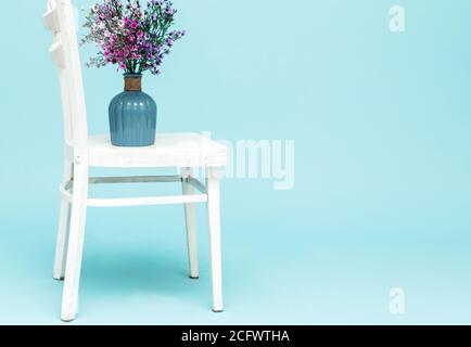 Bouquet of artificial lavender bouquet flowers in glass vase on white chair and blue background. Minimal style interior. Copy space. Stock Photo