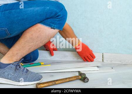 Worker instal plastic skirting board on laminate flooring. Renovation of baseboard at home. Stock Photo