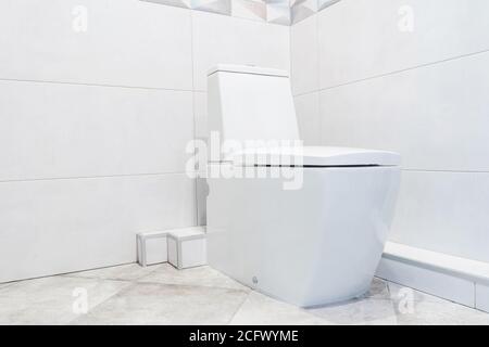 New modern ceramic toilet bowl near grey tiled wall in restroom. Stock Photo