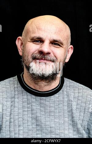 middle-aged bald bearded man smiling on black background Stock Photo