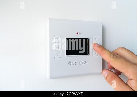 Man hand setting the room temperature on a modern programmable thermostat water heater (boiler). Smart home. Stock Photo