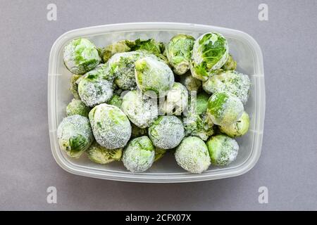 Frozen brussels sprouts in a plastic container for long-term storage. Deep freezing of vegetables. Frozen food vegetables on grey background. Stock Photo