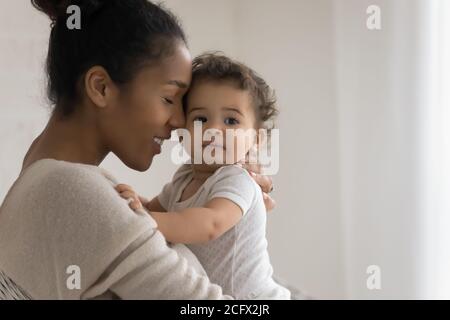 Bonding mixed race young mommy cuddling sweet little kid. Stock Photo