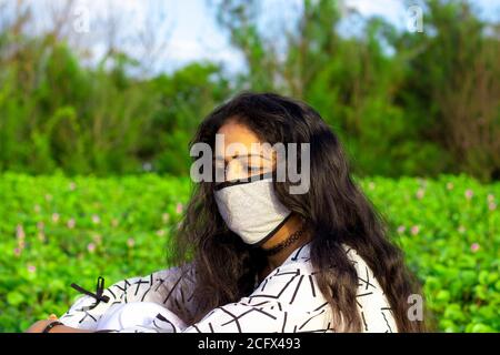 Portrait of a stylish young girl sitting in the nature and wearing face mask Protection against disease, coronavirus. Stock Photo
