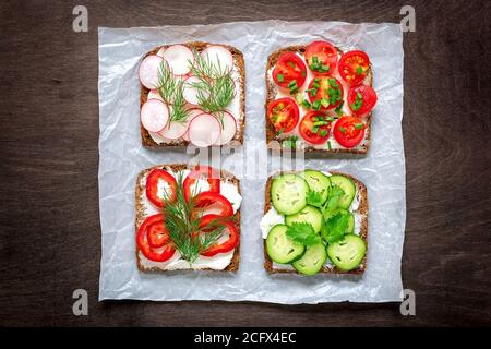 Variety of sandwiches for breakfast - slice of whole grain dark bread, red pepper, cream cheese, cucumbers, radishes, cherry tomatoes, garnished with Stock Photo