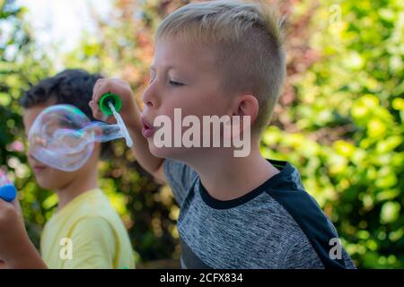 Blond boy in grey shirt blowing bubbles in nature Stock Photo