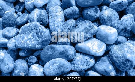 Wet sea pebbles toned in classic blue color. Abstract natural trendy background. Zen and calm concept. Close-up. Selective focus Stock Photo