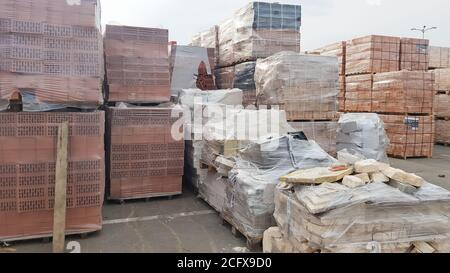 Red perforated bricks with rectangular holes on wooden pallets in an open-air warehouse ready for sale. New bricks on pallets at a hardware store Stock Photo