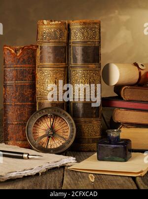 Antique books, compass, ink pot, quill pen and papers on table Stock Photo