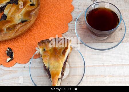 home cooking, a pie, a slice of apple pie filled with cherries and walnuts, a cup of tea and a handful of peeled walnuts on a wooden table Stock Photo