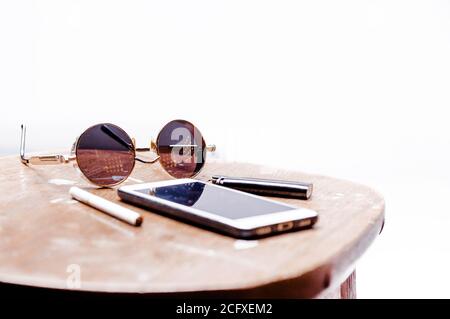 Cigarettes, sunglasses, glasses and a telephone lie on a wooden table on a white background. Brutal man set Stock Photo