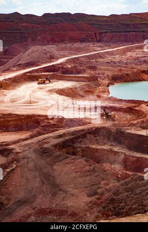 Bauxite open cast (open cut) mining. Color aluminium ore quarry. Blue quarry lake. Dump (quarry) tracks and excavators. Stock Photo