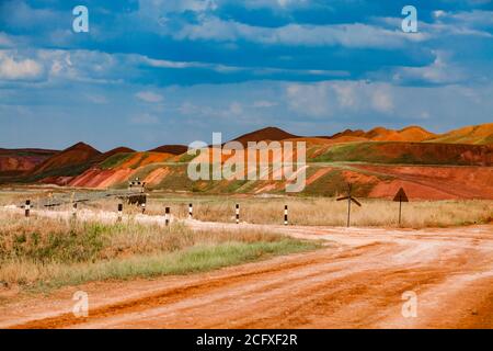 Aluminium ore quarry. Bauxite clay open-cut mining. Heaps of color minerals. Empty quarry stones rock with green grass. Blue sky background. Stock Photo