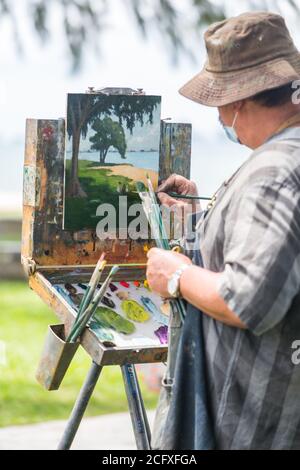 Close up vertical view of a big-size professional painter artist doing his painting outdoor near the beach. Stock Photo