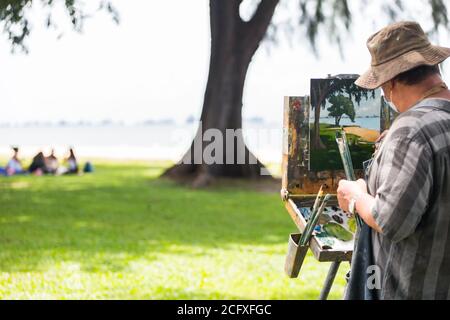 A painter is painting a nature scenery - in-front was a group of women having panic and conversation on a sunny tropical afternoon. Stock Photo