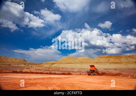 Orange quarry truck in the bauxite mine. Open-cut mining of aluminium bauxite ore. Scenic landscape with working machine. Blue sky with clouds Stock Photo