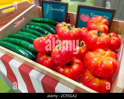Artificial cucumbers and tomatos in a wooden box as a market design on the background of other vegetables and fruits, soft focus. Stock Photo