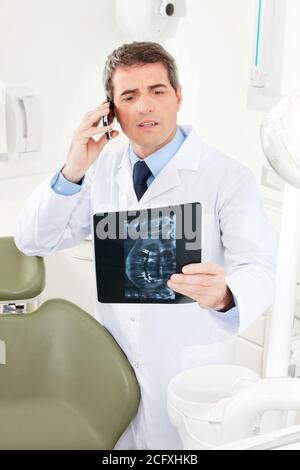 Dentist on the phone with x-ray image of dentures in hand Stock Photo