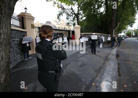 An officer from the PSNI watches residents during a protest outside the Chinese Consulate, Belfast, amid a dispute over the construction of a boundary wall and entrance gate which have been built without planning permission. Stock Photo