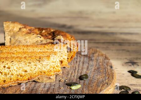 Fresh baked pumpkin bread and seeds on cutting board closeup. Homemade pumpkin bread on rustic wooden table. Home bread-making concept Stock Photo