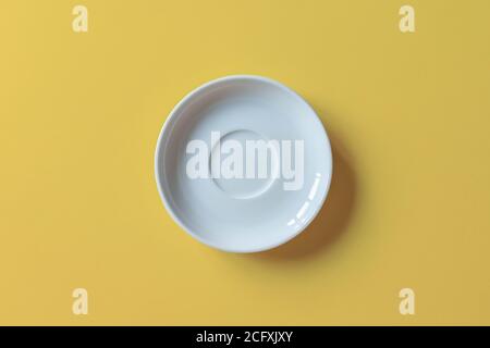 White plate for cake placed on yellow background. Empty ceramic round plate isolated on yellow background. Flat lay. Top view. Stock Photo