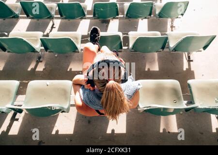 top view of a female athlete sitting at an old stadium listening to music and resting after exercising Stock Photo