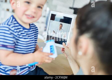 Mother with child in video chat as online consultation with a pediatrician Stock Photo