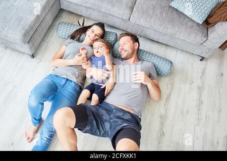 Happy family with toddler lying on pillows in front of sofa in living room Stock Photo