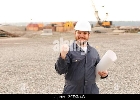 Happy foreman holding blueprints papers on construction site. Stock Photo
