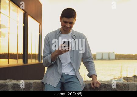 Young man uses a phone outdoor. Writing a message Stock Photo