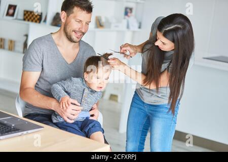 Mother cuts her son's hair with the help of father and tutorial online Stock Photo