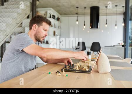 Concentrated man playing chess in video chat online at home in the living room Stock Photo