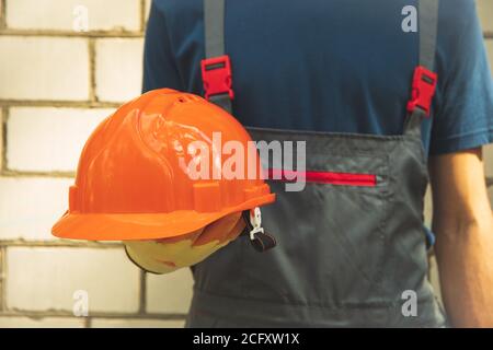 Man in overalls holds safety helmet outdoor Stock Photo