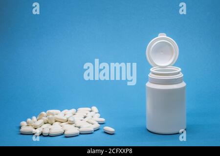 White bottle with a pile of oval tablets on a blue background. Background Stock Photo