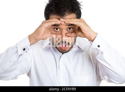 Closeup portrait of a young handsome happy man peeking through his fingers like binoculars, searching for something, looking to the future at the came Stock Photo