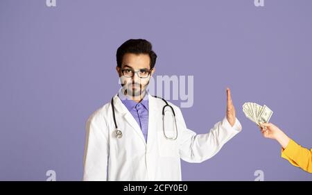 Reducing corruption in health sector. Serious Indian doctor saying no to bribe from female patient, lilac background Stock Photo