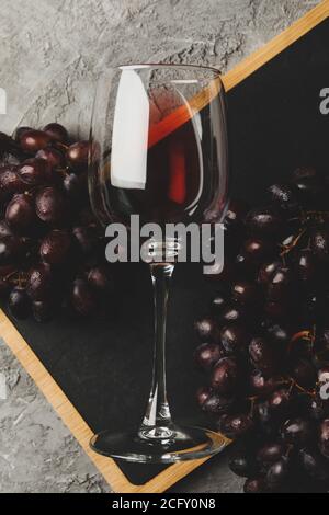 Board with grape and glass of wine on gray background Stock Photo