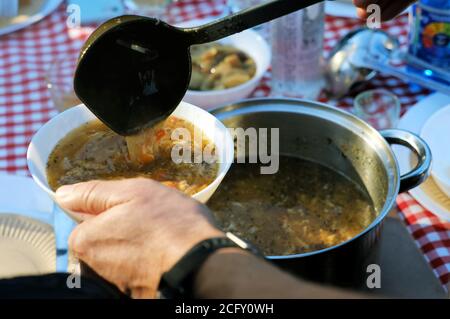 Man pouring delicious, traditional polish soup flaki 'tripe' into a bowl at a garden party Stock Photo