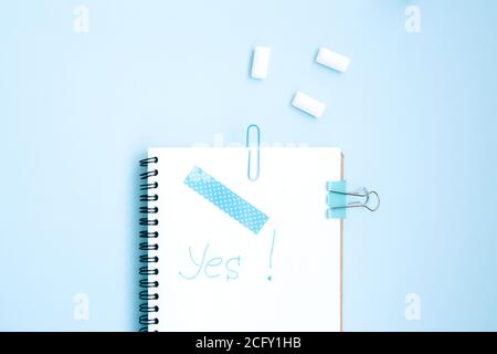 White open notebook with blue paper clip, clip and piece of scotch tape and gum on blue background. Inscription on paper consent. Blue set stationery Stock Photo