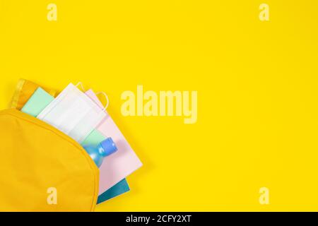 Education, learning, back to school during pandemic. Top view to backpack with school supplies, hand sanitizer, protective mask on yellow background Stock Photo