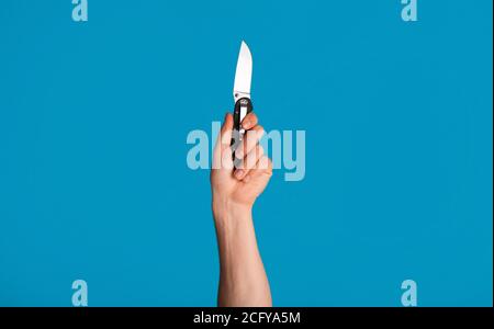 Unrecognizable young man holding pocket knife on blue background, closeup of hand Stock Photo