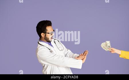 Stop corruption in healthcare. Indian doctor refusing bribe from patient on violet background Stock Photo