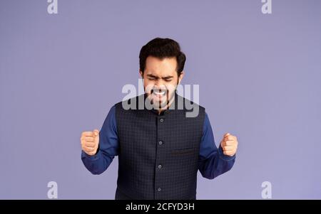 Furious Indian man clenching fists in anger and screaming on lilac background Stock Photo