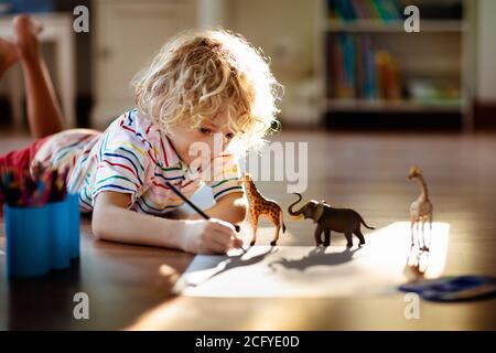 Child shadow drawing animals. Kids play at home. Fun crafts for kindergarten children. Little boy painting giraffe and elephant in sunny bedroom. Game Stock Photo