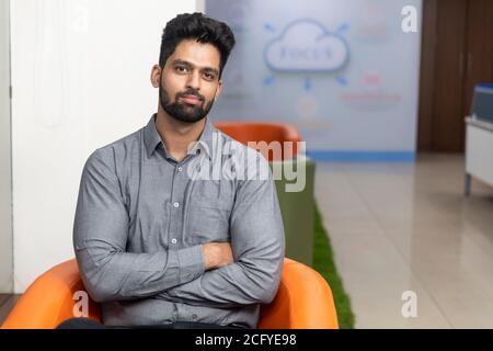 Portrait of young successful Indian business man sitting on couch with folded arms, Corporate environment. Stock Photo