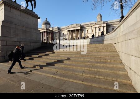 People seen walking up the steps towards the north terrace on Trafalgar Square London towards the National Gallery in the background against blue sky. Stock Photo