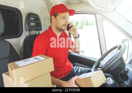 package delivering - delivery man using mobile phone while sitting in van Stock Photo