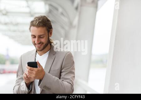 Portrait of handsome curly businessman in casual wear holding smartphone and smiling.Successful manager using mobile phone apps,texting message Stock Photo